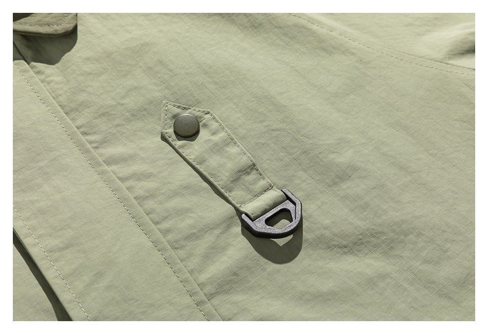 Close-up of an olive-green jacket's stitched fabric loop with a dark metal ring and snap.