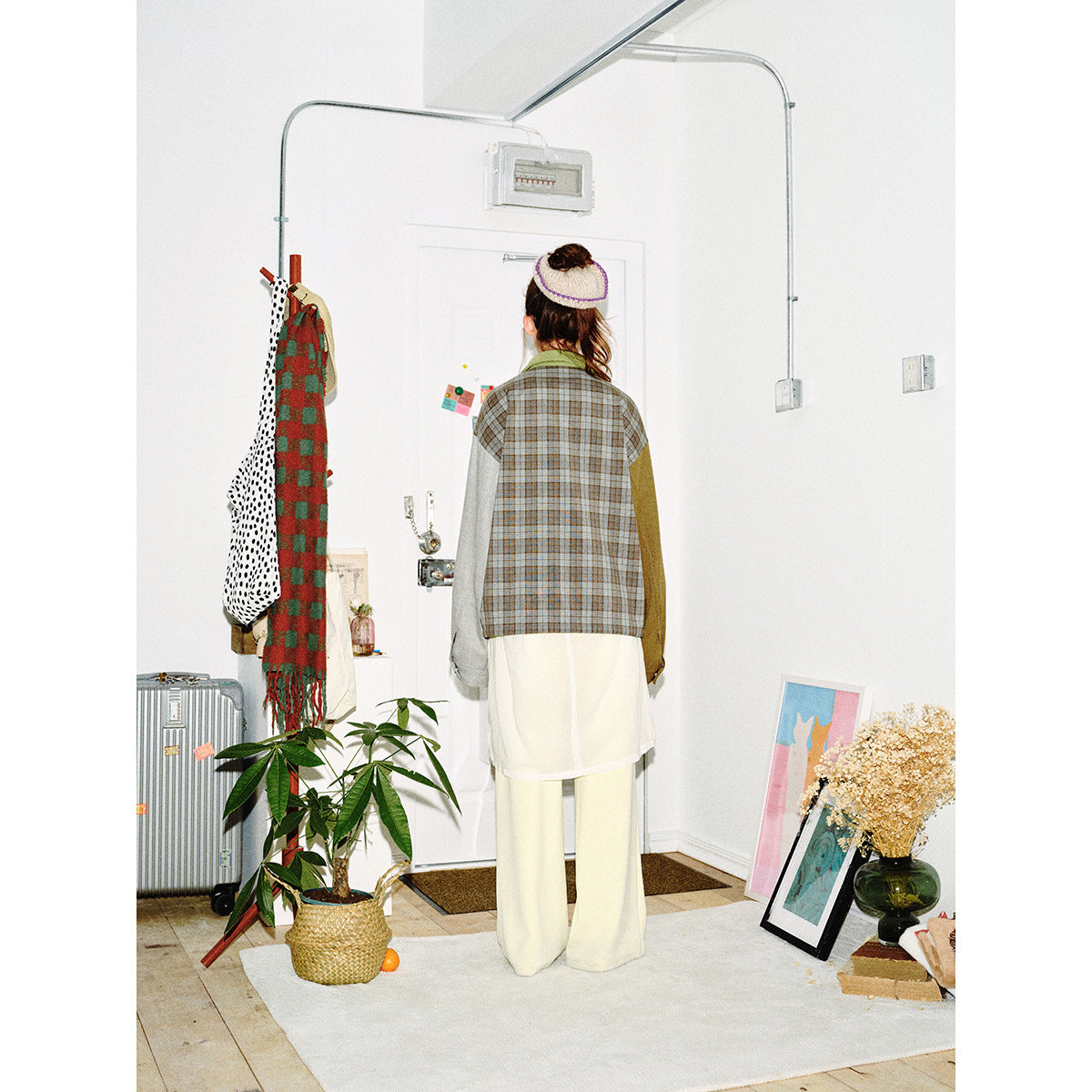 Rear view of a model wearing a jacket with a gray-brown plaid back, contrasting sleeves, and a green collar.