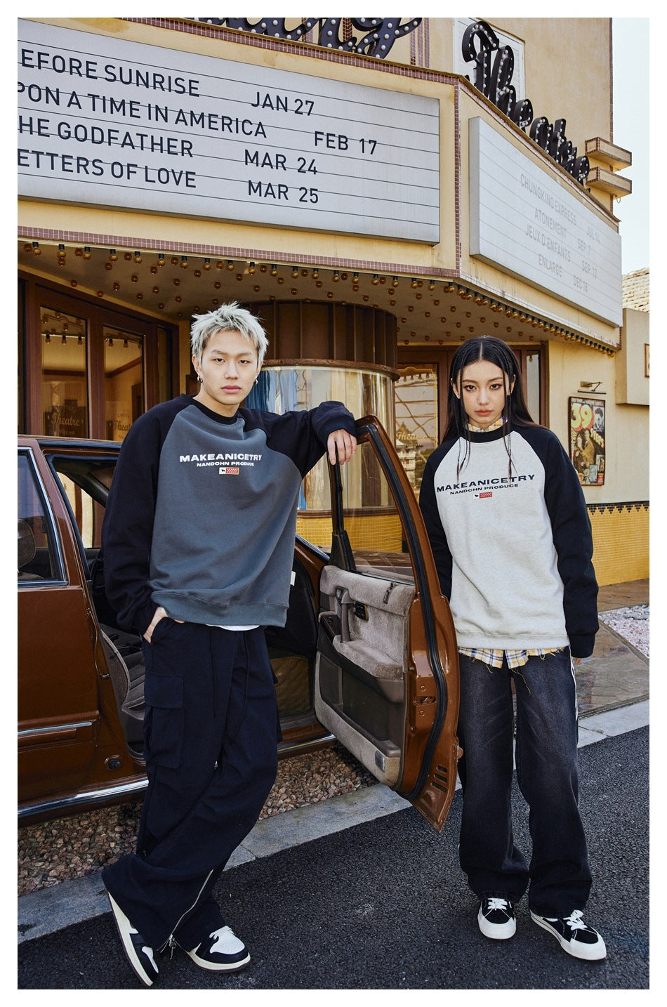 Two models show gray and cream raglan sweatshirts with black sleeves outside a theater.