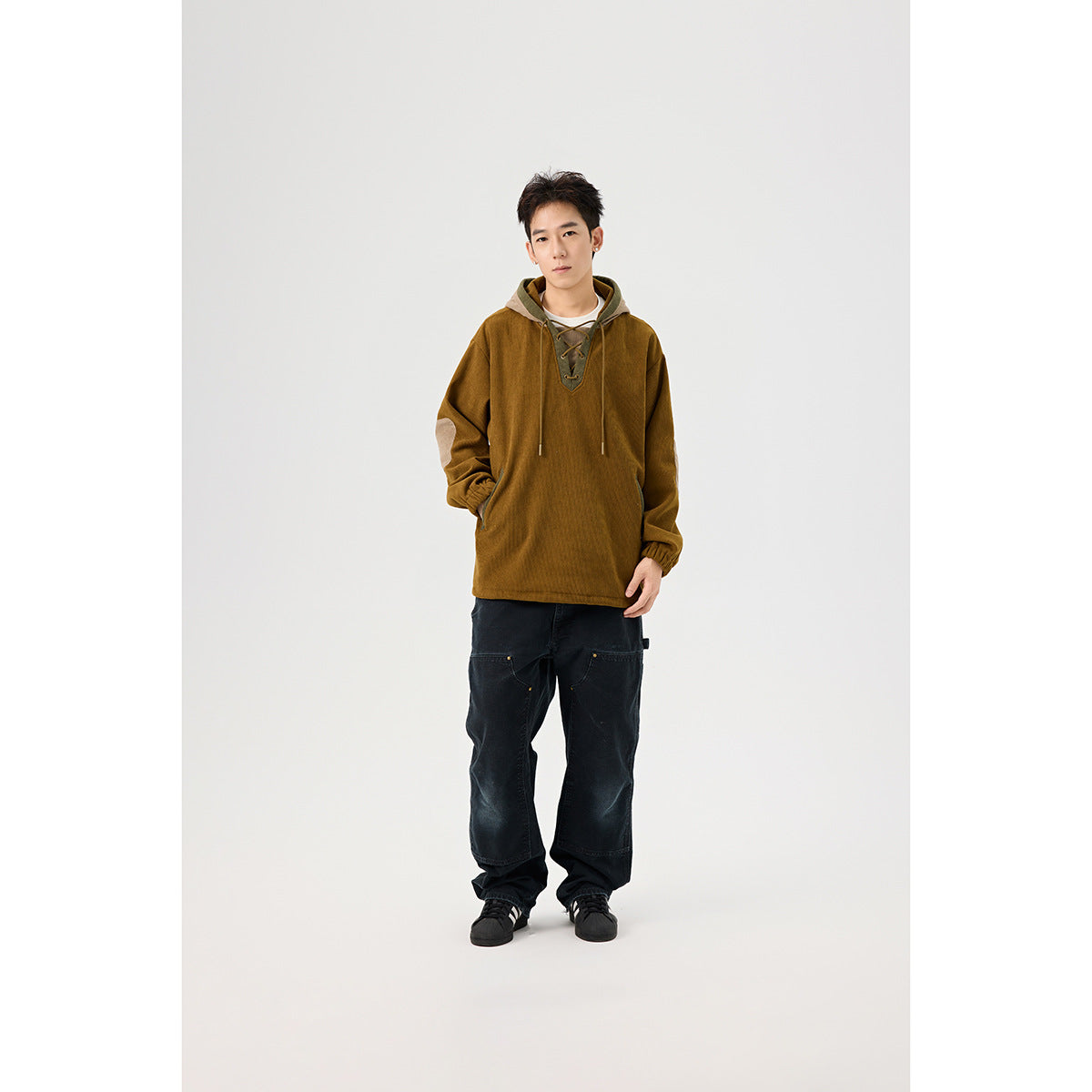 Full-length front view of a model wearing a mustard-brown hooded pullover with a lace-up neckline and black wide-leg pants.