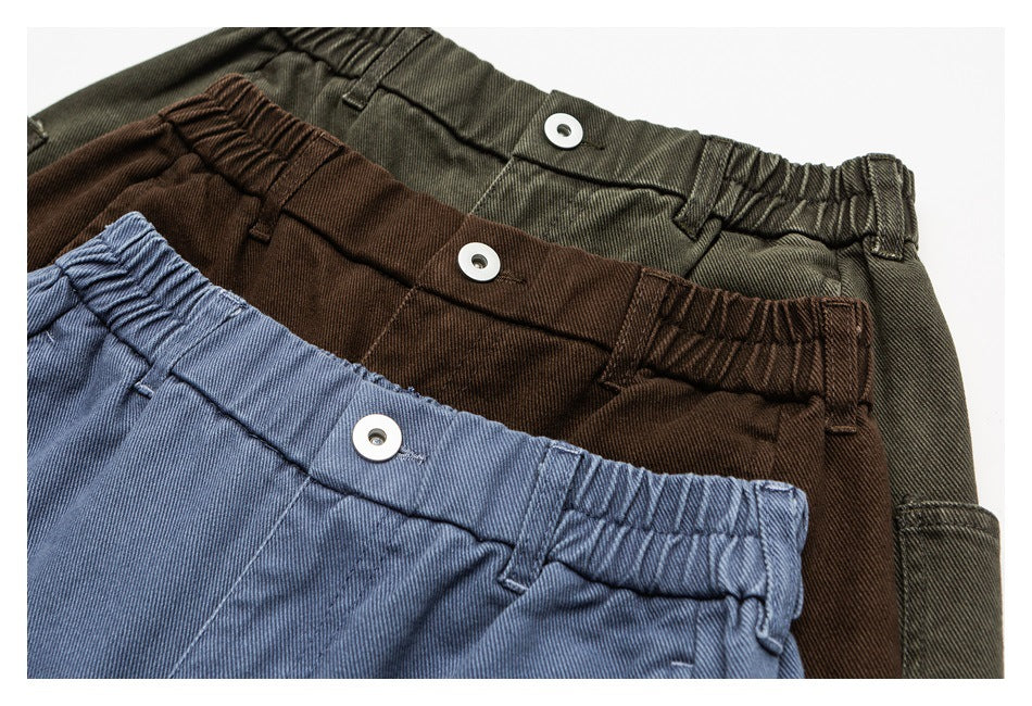 Close-up of blue, brown, and olive pants showing elasticized waistbands and button closures.