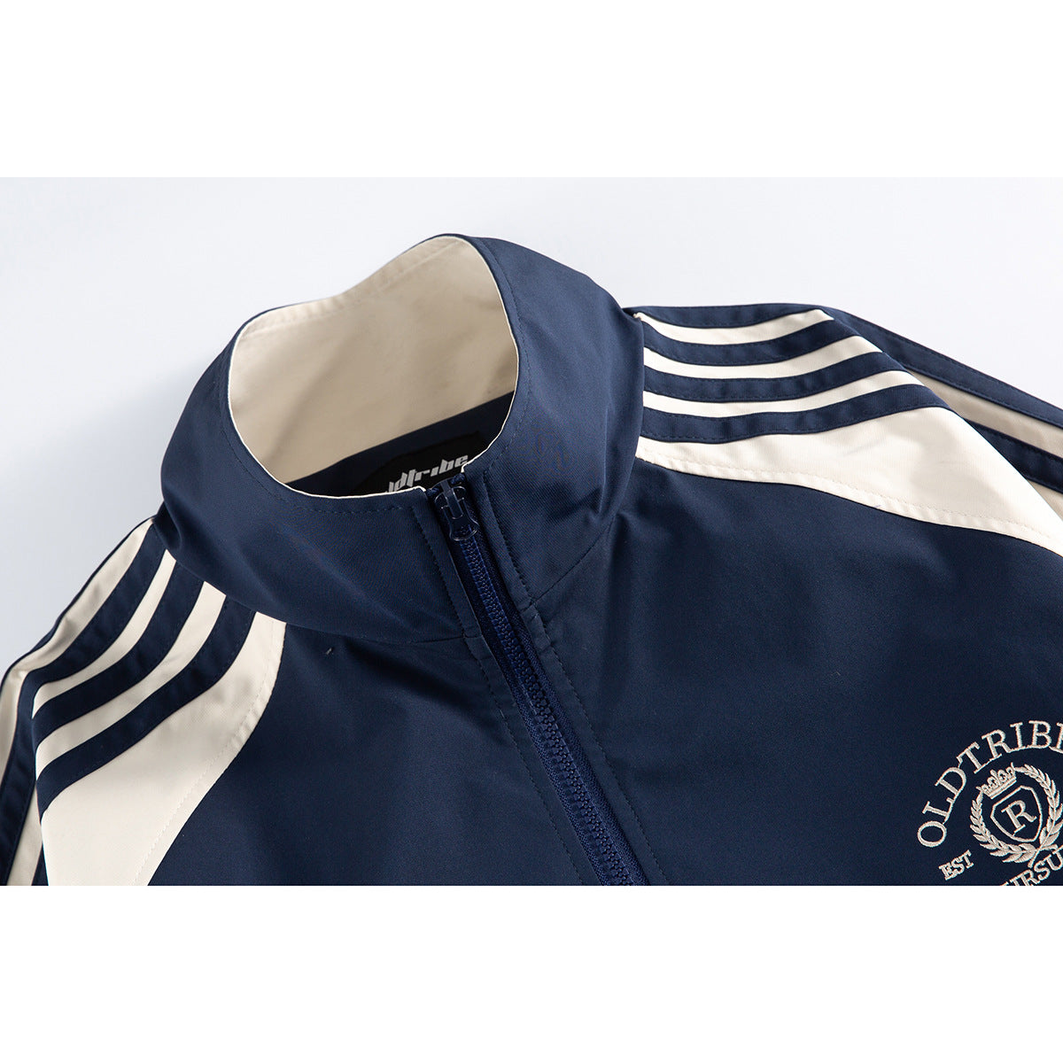 Close-up of a navy zip-up jacket with cream shoulder stripes, a stand collar, and a cream chest crest.