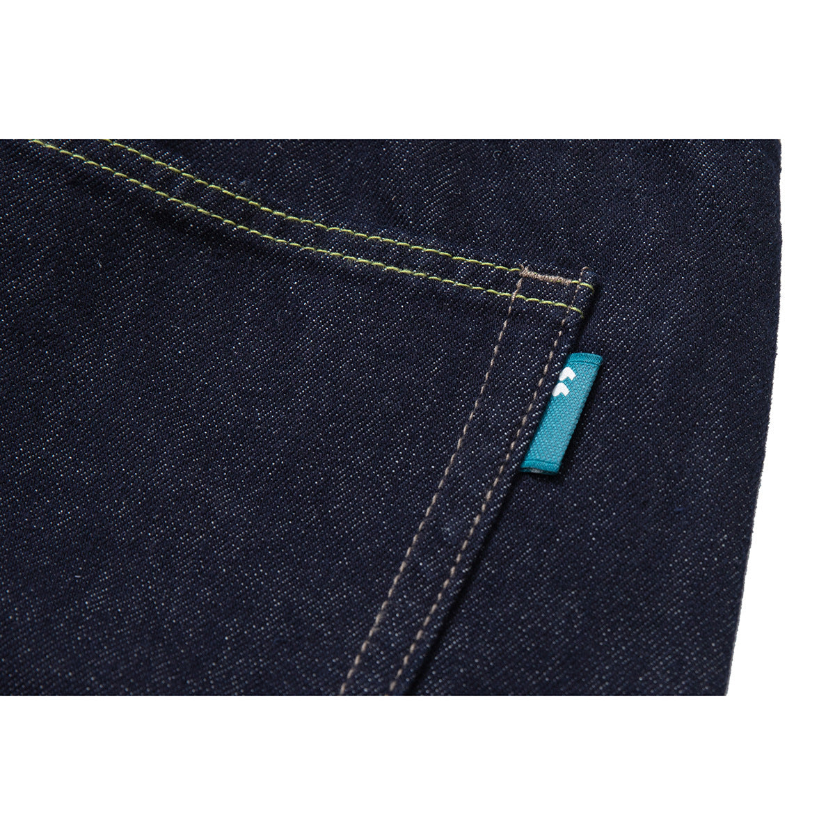 Close-up of dark indigo denim with contrast stitching and a small turquoise fabric tab.