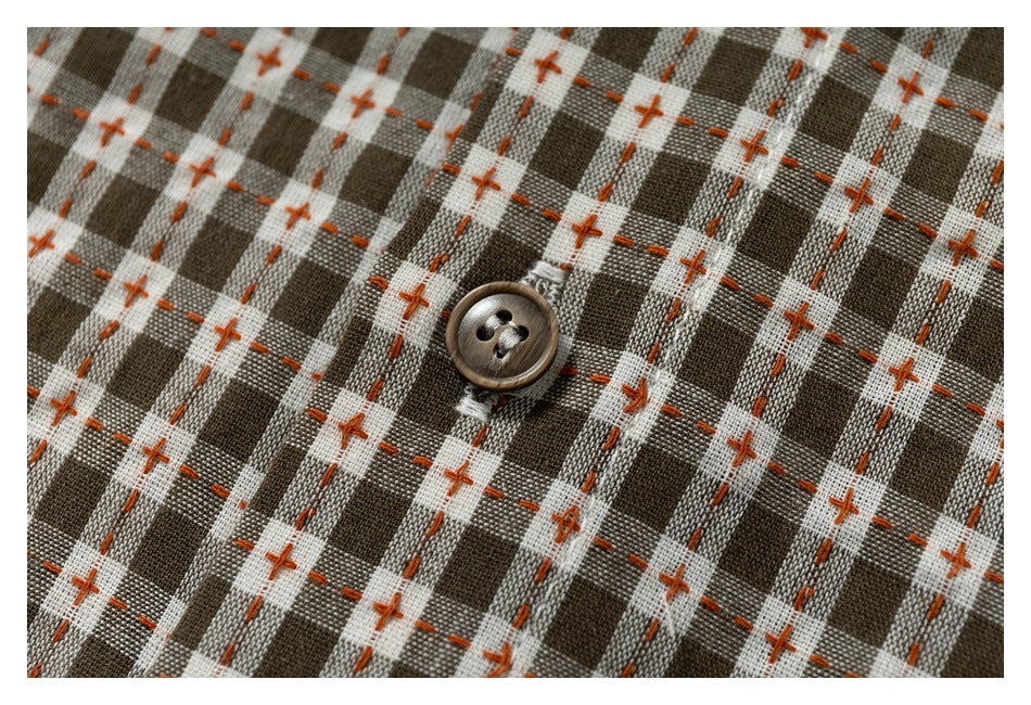 Close-up of a brown button on brown-and-cream checked shirt fabric with orange cross-stitch accents.
