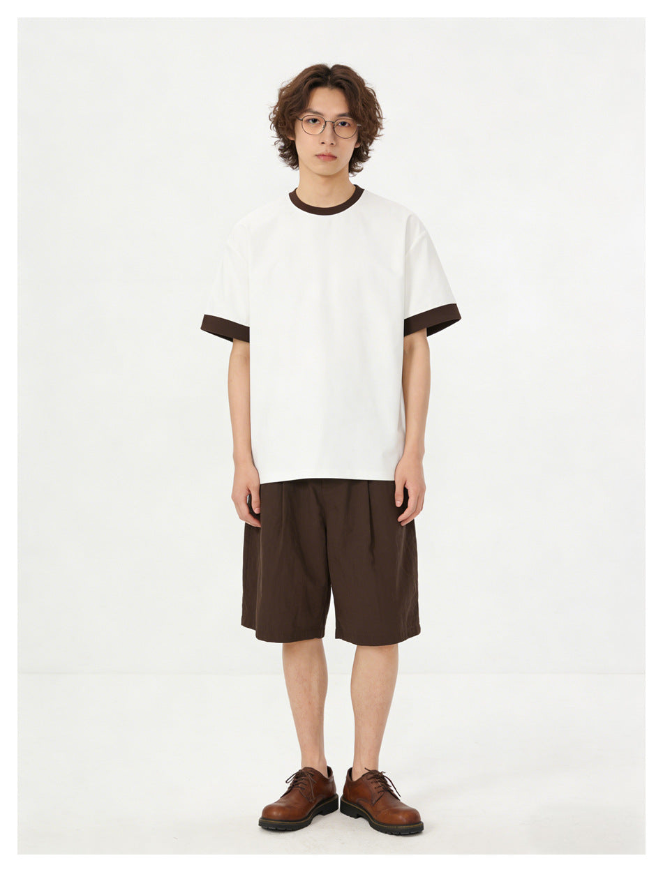 Model wearing a white short-sleeve T-shirt with dark brown collar and sleeve trim, paired with brown shorts.