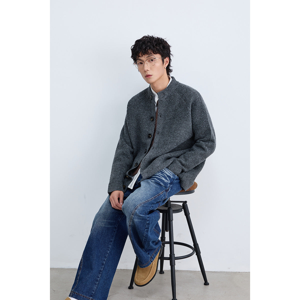 Seated model wearing a charcoal gray button-front cardigan with blue jeans.
