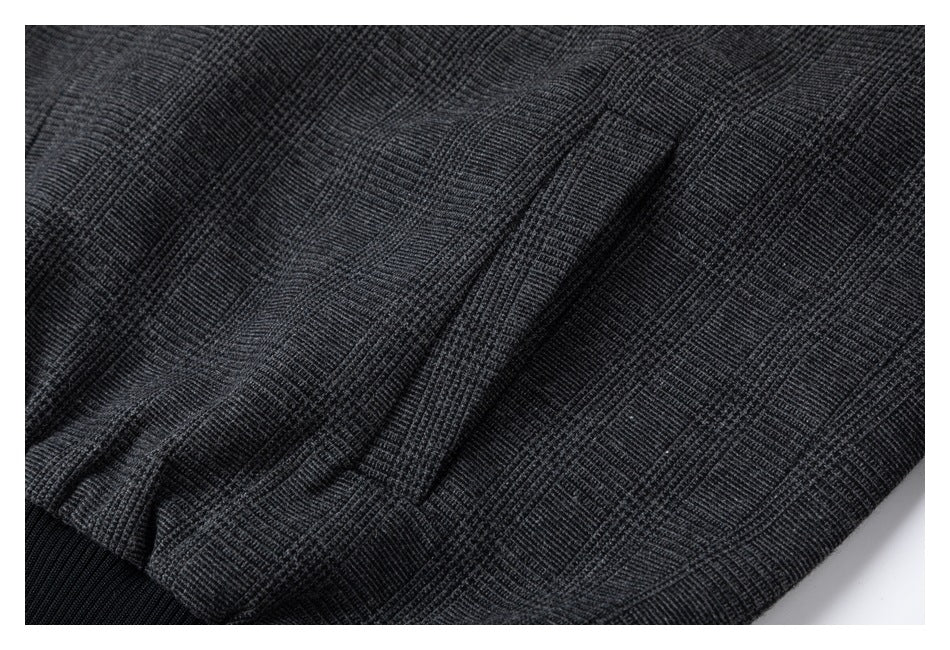 Close-up of charcoal plaid jacket fabric gathered above a black ribbed hem.