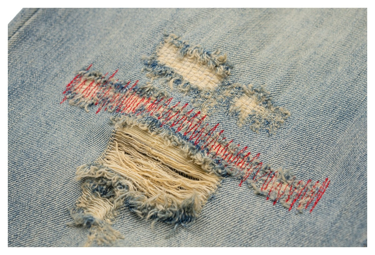 Close-up of distressed light blue denim with frayed holes and red repair stitching.