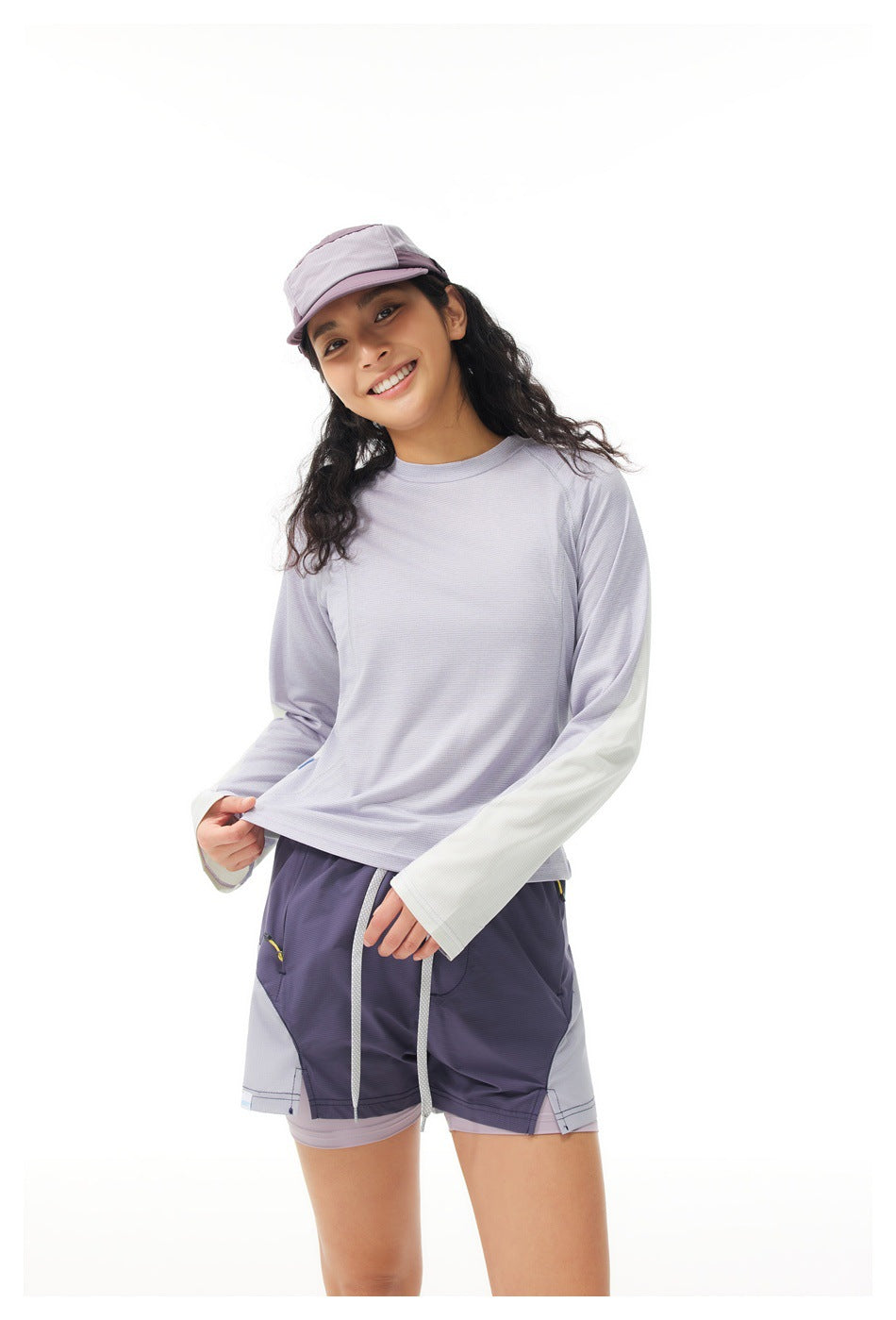 Woman wearing a pale lavender long-sleeve athletic top with white sleeve panels and coordinating shorts.