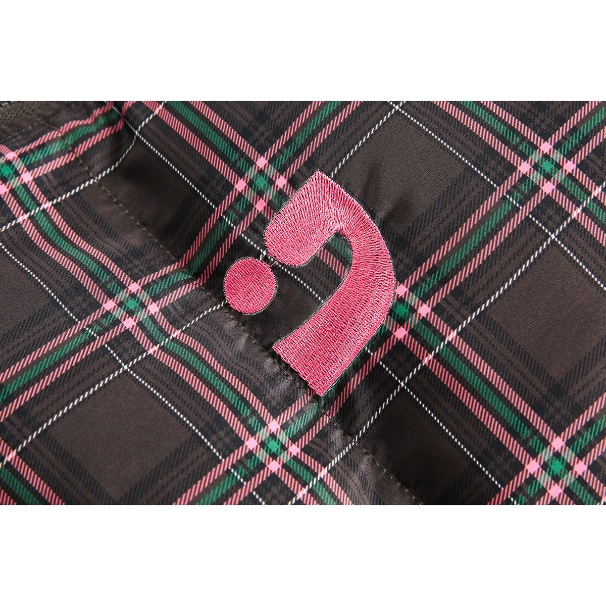 Close-up of a pink embroidered emblem on dark gray plaid jacket fabric with pink and green lines.
