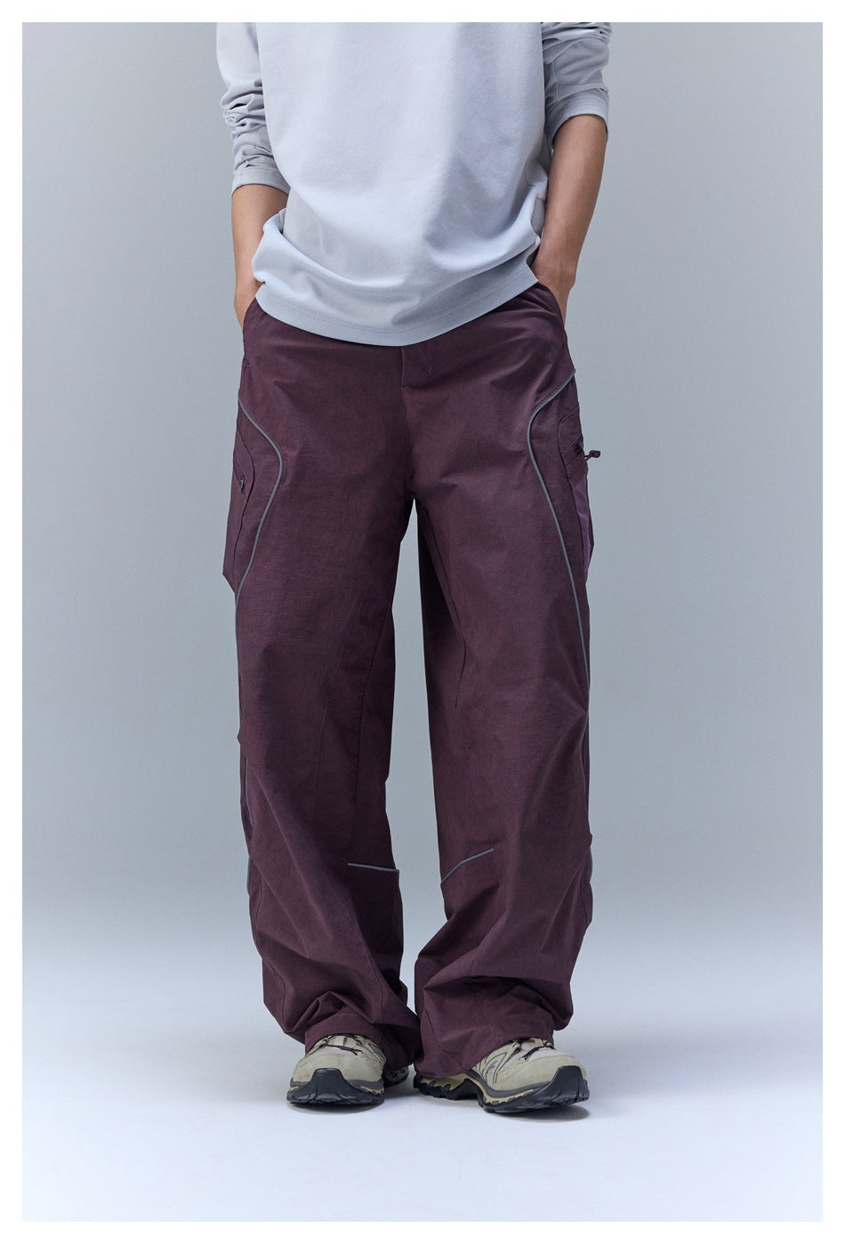 Person wearing purple wide-leg cargo pants with curved piping, light gray top and trail sneakers, front view