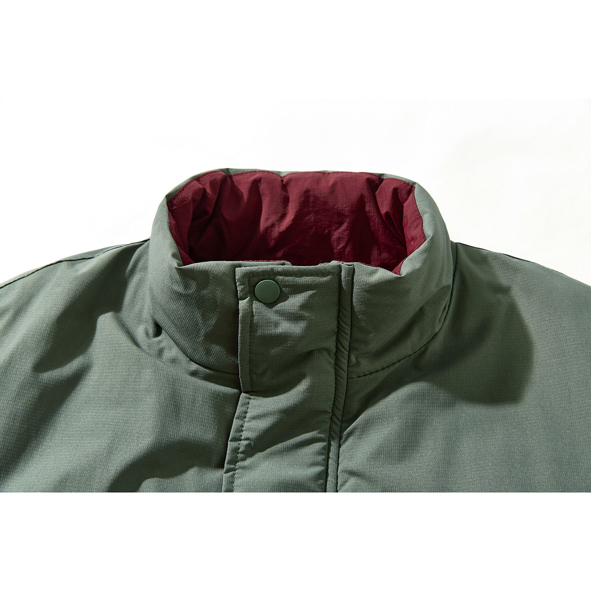 Close-up of a sage green jacket’s high collar, burgundy lining, and snap-button storm flap.