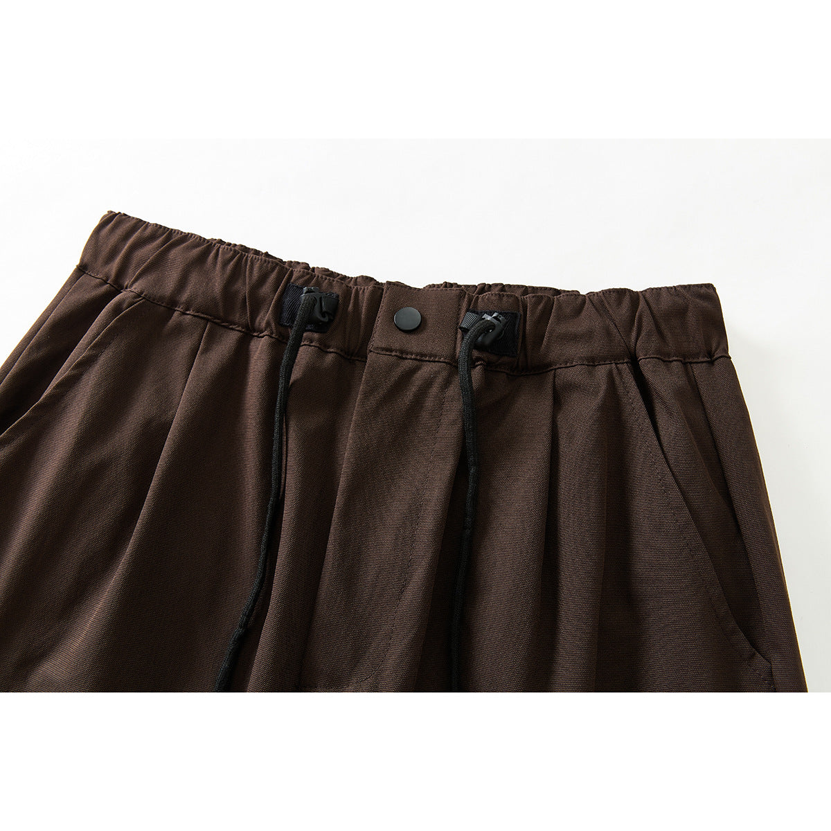Close-up of brown wide-leg trousers showing the gathered waistband, black drawcords, and front button.
