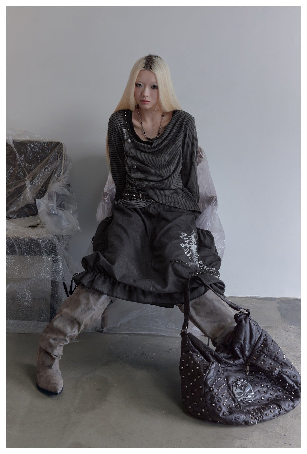 Seated model wearing a charcoal striped asymmetrical top and a voluminous black graphic skirt.