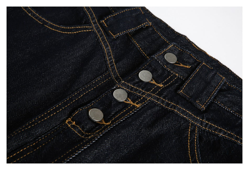 Close-up of dark indigo jeans showing the waistband, belt loop, and silver button fly with golden stitching.