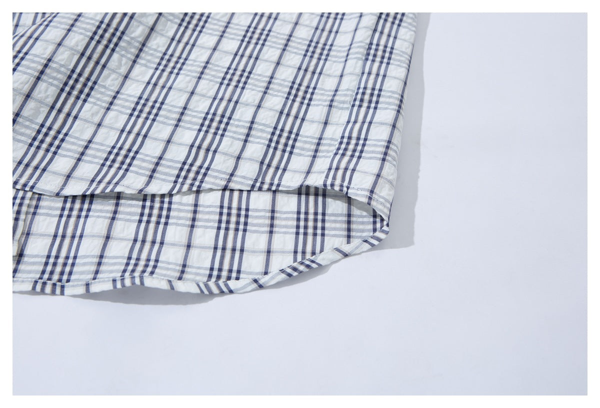Close-up of the curved bottom hem of a white shirt with navy and gray plaid.