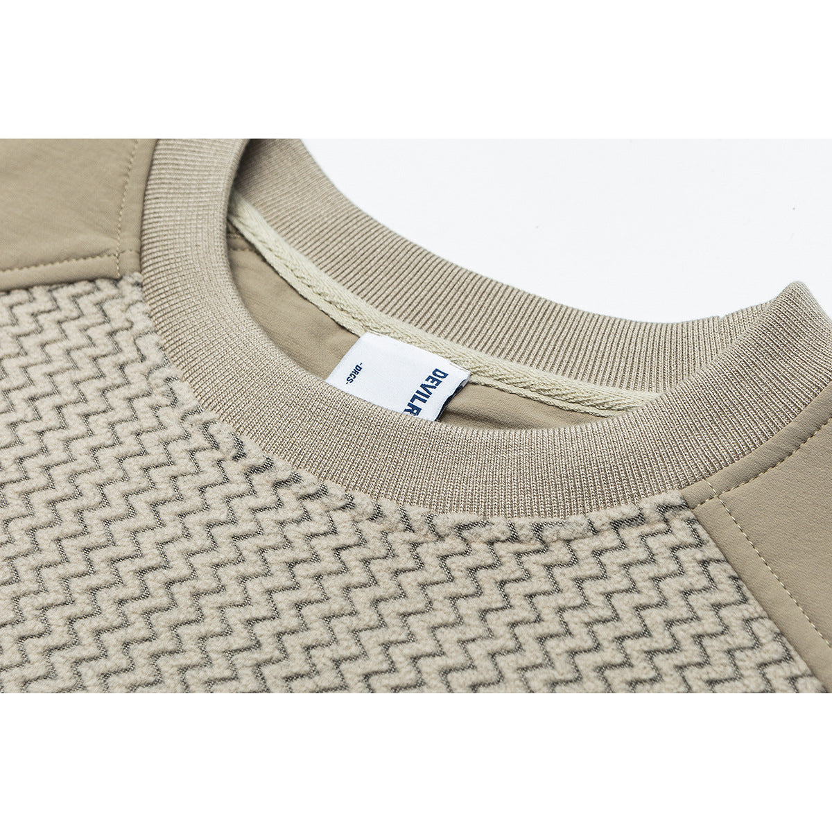 Close-up of a beige crewneck collar, ribbed neckline, patterned fabric, and a sewn brand label.