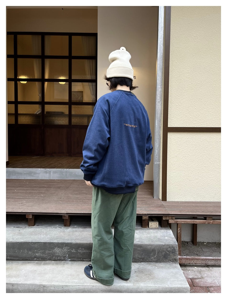 Back view of a person in a blue crewneck sweatshirt, green pants and cream beanie standing outside a building