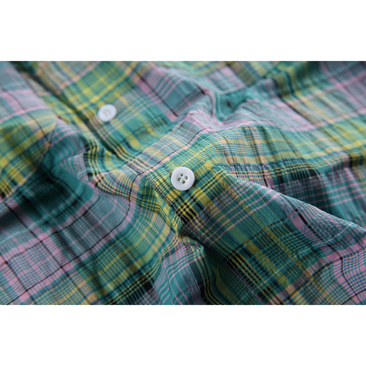 Close-up of white buttons and the teal, pink and yellow plaid fabric on the shirt.