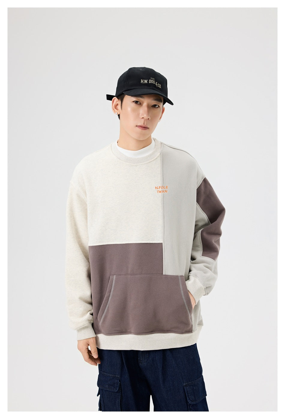 Model wearing an oatmeal, taupe and gray color-block crewneck sweatshirt with hand in the front pocket
