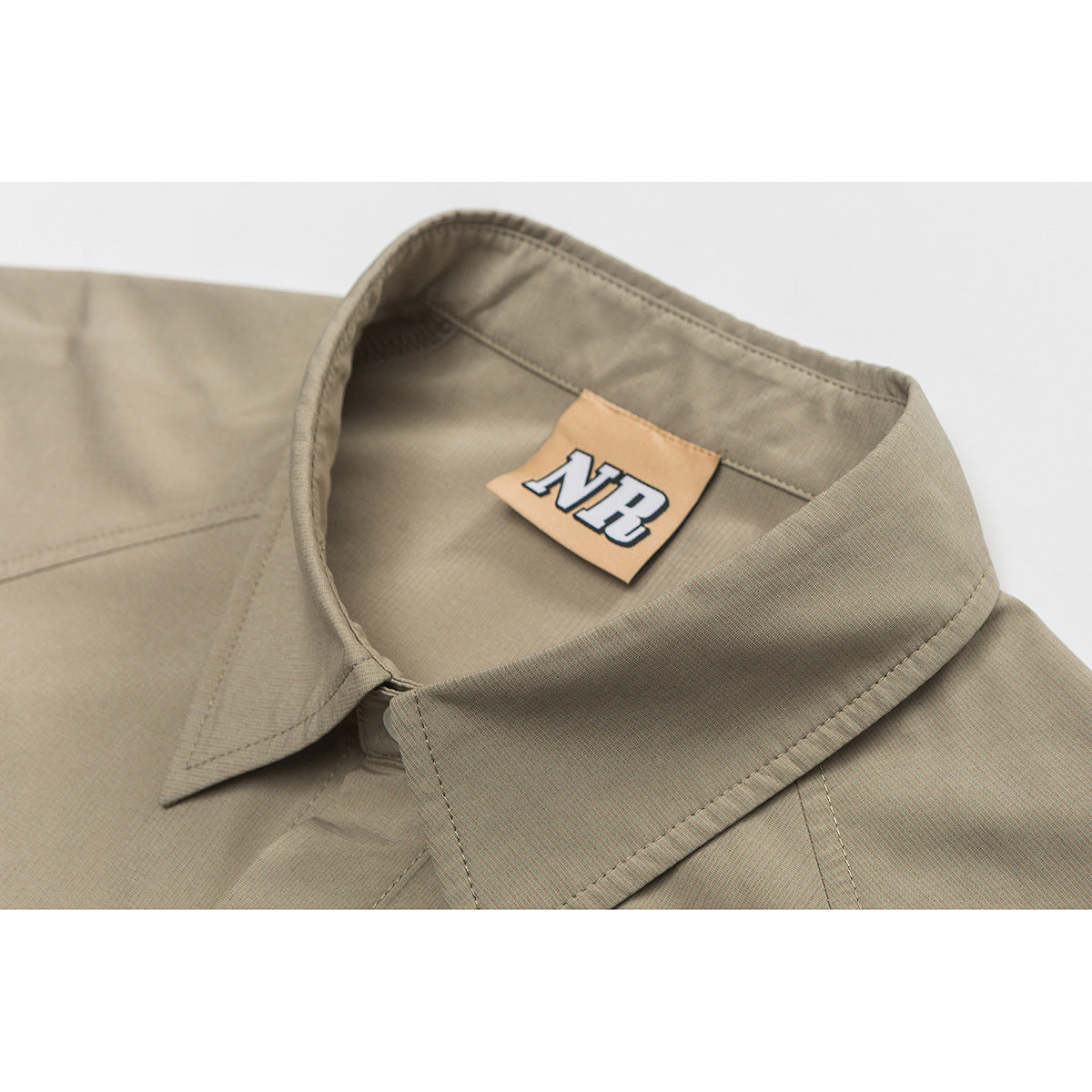 Close-up of a taupe shirt collar and inner neck label marked “NB.”