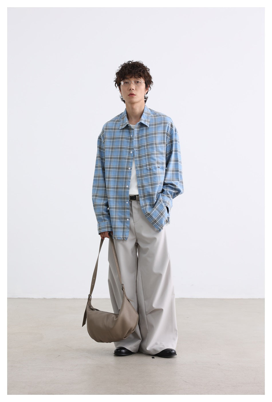 Full-length model wearing a blue plaid button-up shirt with a frayed chest pocket and hem, styled with light trousers.