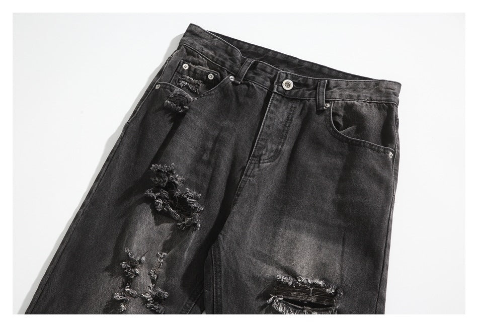 Angled front view of black washed jeans with a button fly, front pockets and distressed tears.