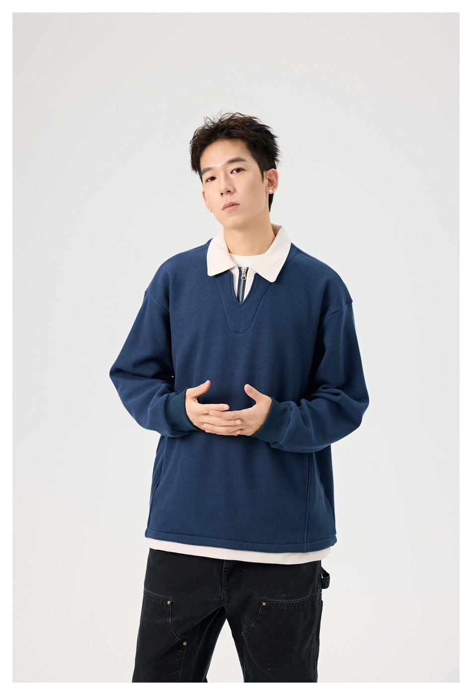 Model wearing an oversized navy pullover with a cream collar, short zip neckline and cream layer showing at the hem.