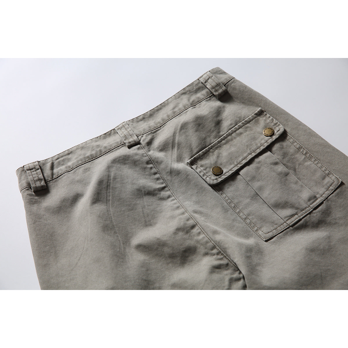 Close-up of gray work pants showing a rear flap pocket with two metal buttons.