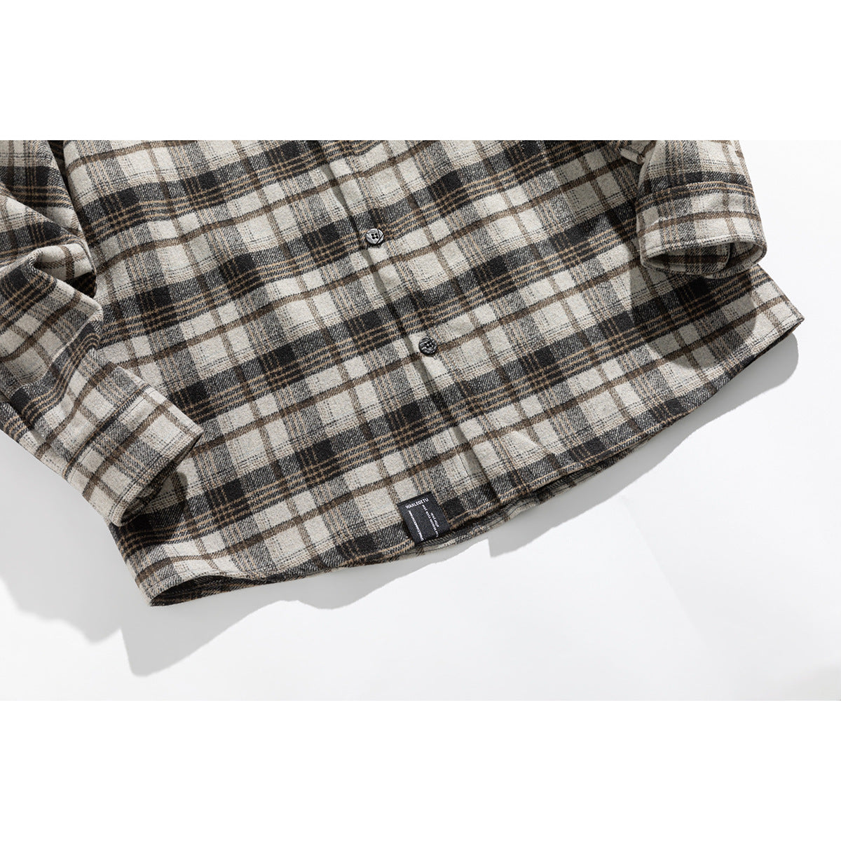 Cropped view of a cream, gray, and brown plaid shirt front, hem, and buttoned cuffs.