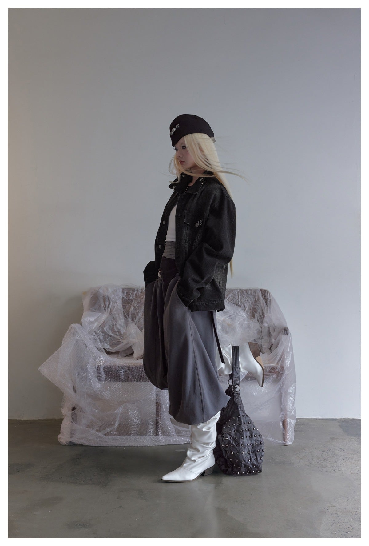 Full-length side view of a model wearing an oversized black denim jacket, dark trousers, and white boots.