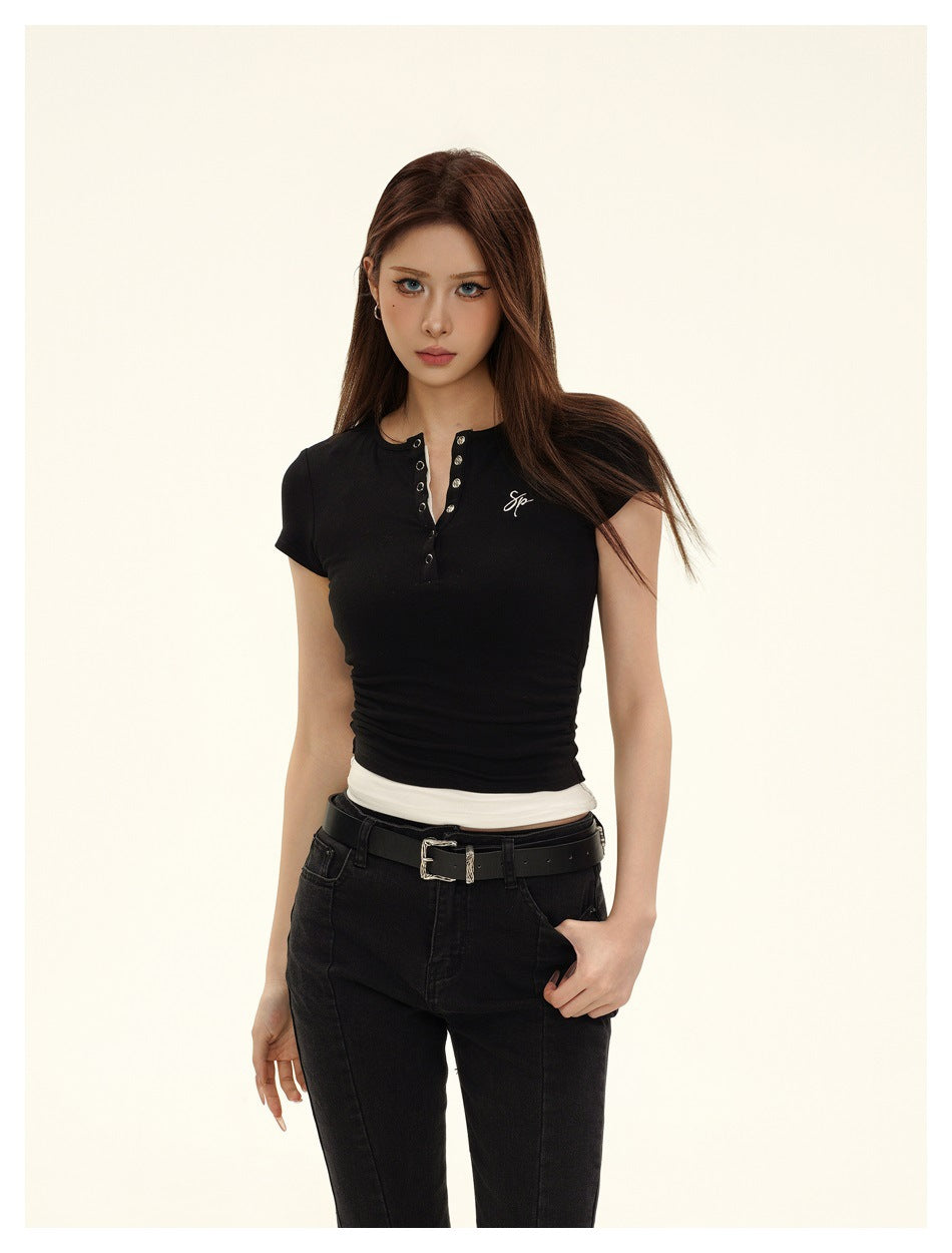 Framed front view of a model in a fitted black short-sleeve top with a metal-eyelet neckline and black jeans.
