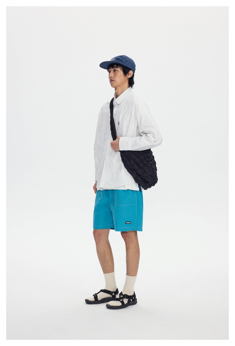 Model wearing bright turquoise shorts with patch pockets, a white shirt, and a dark shoulder bag.