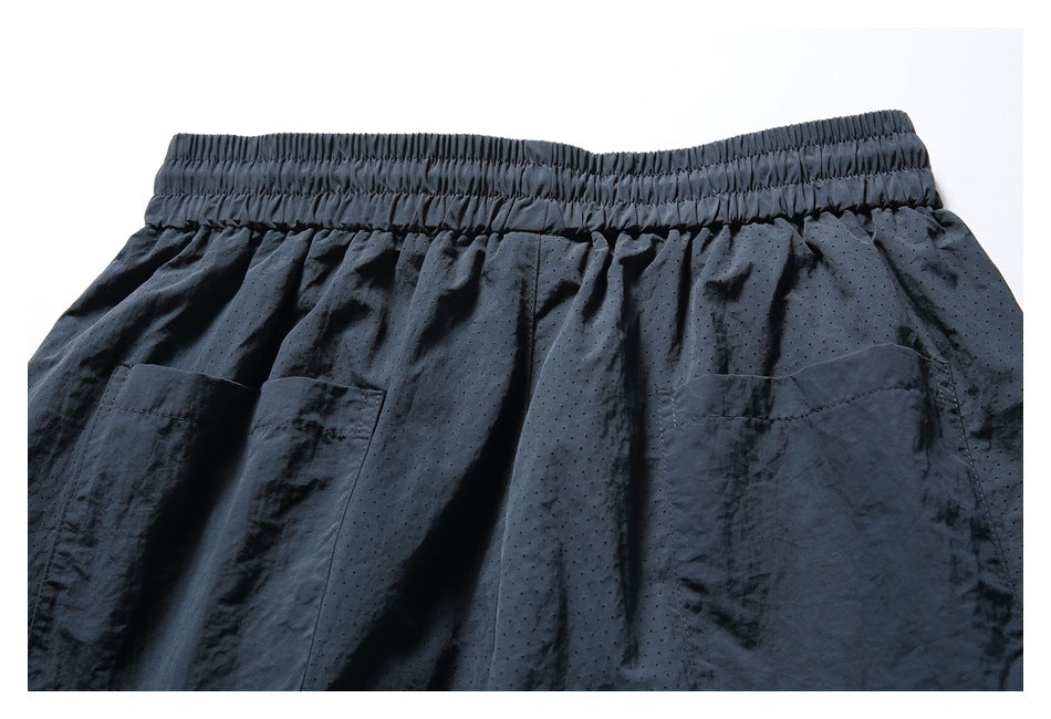 Upper front of black shorts with an elastic waistband, two patch pockets, and perforated fabric.