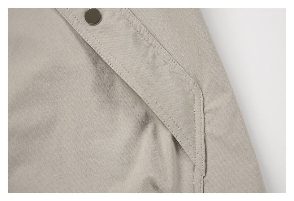 Close-up of a light taupe garment with a diagonal stitched flap and dark snap button.