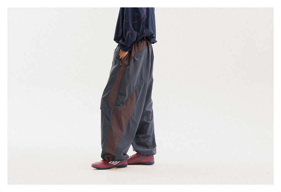 Side view of a cropped model wearing loose charcoal trousers with brown contrast panels.