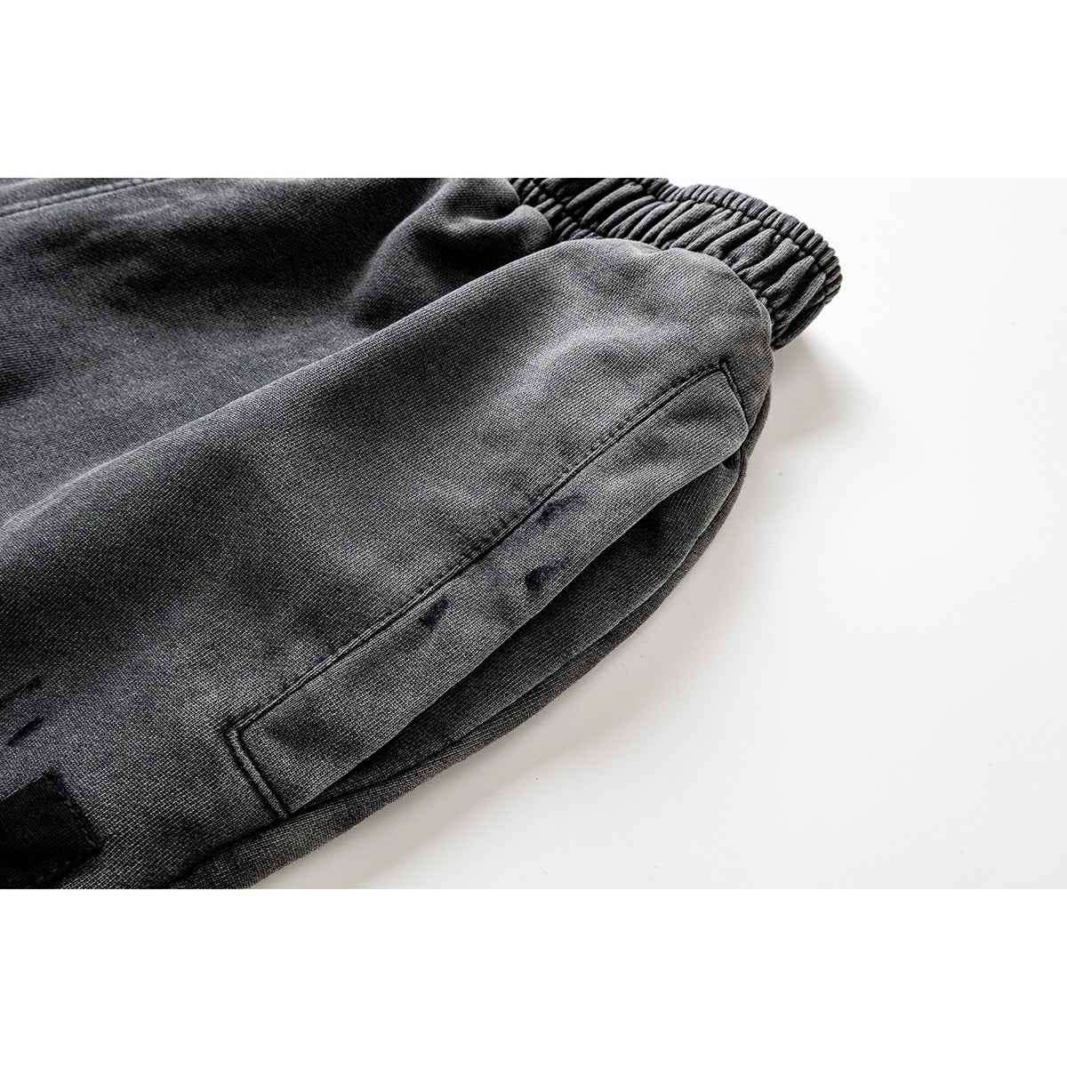 Close-up of charcoal-gray pants showing a stitched side pocket and elastic ankle cuff.