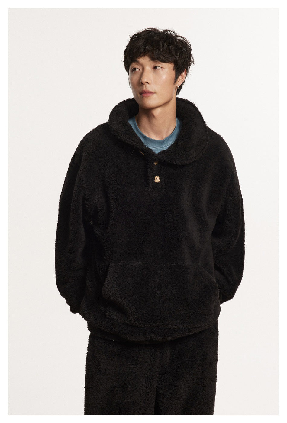 Front view of a model wearing a black plush pullover with a wide collar, button placket and large pouch pocket.