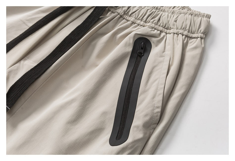 Close-up of a black vertical zip pocket on light beige shorts beside the gathered waistband and drawcord.