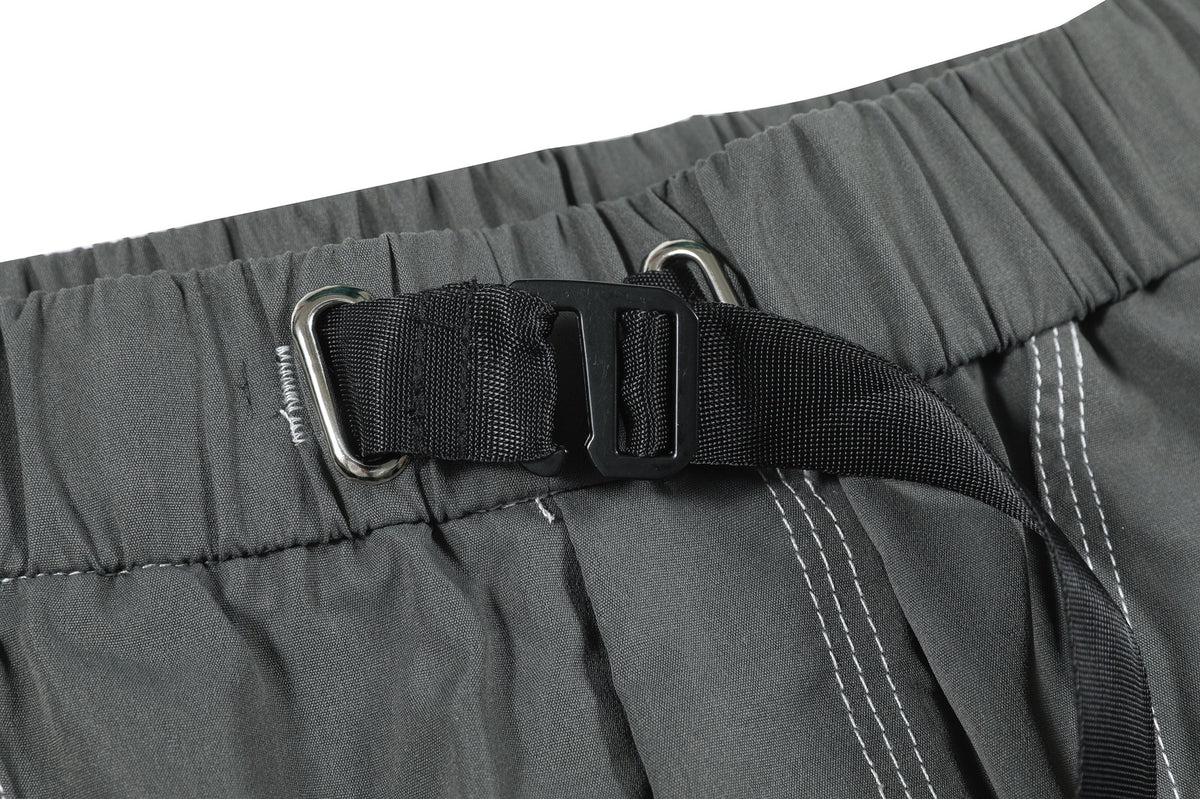 Detailed view of charcoal gray pants with a gathered waist, black buckle strap, metal loops and white stitching.