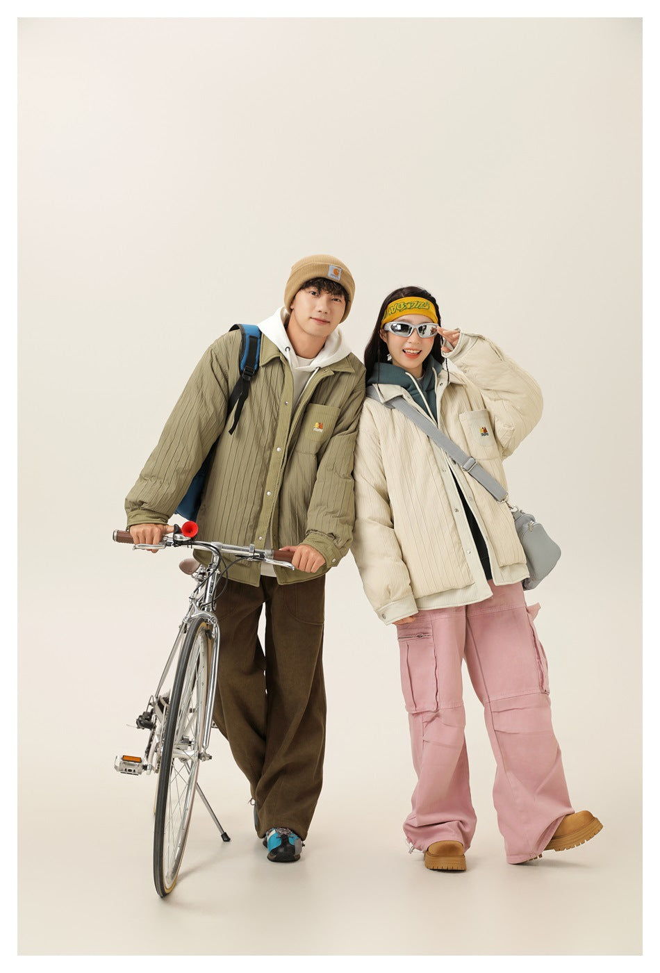 Two models pose beside a bicycle in olive and cream quilted jackets, shown with casual layered outfits.