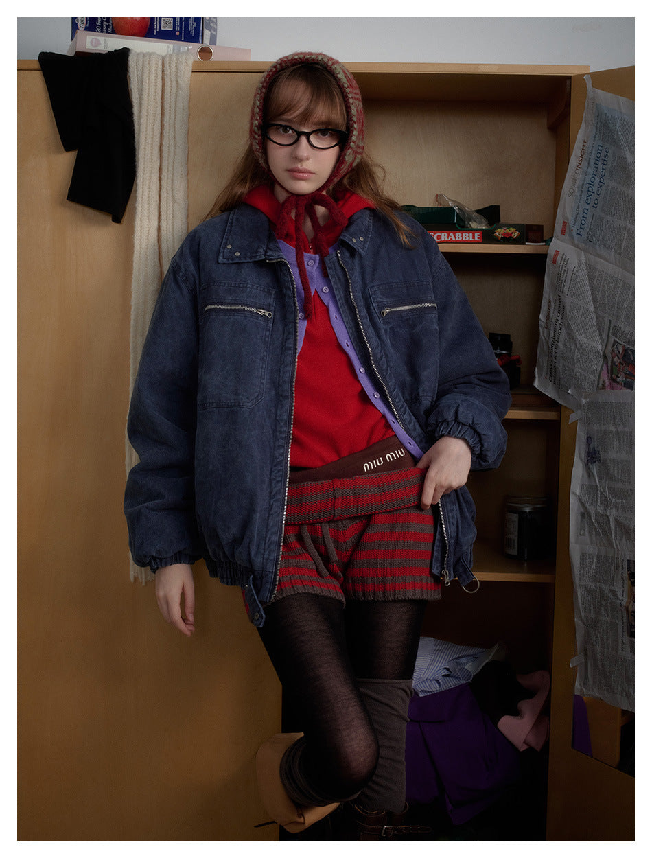 Model wearing a dark indigo zip-front jacket with chest zip pockets, layered over a red top and patterned shorts.