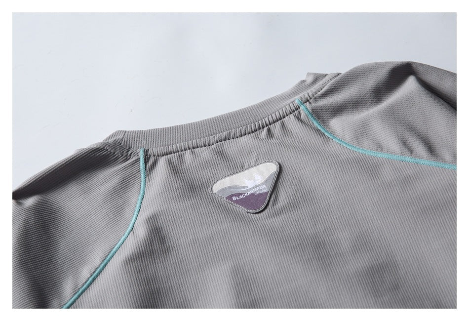 Upper back of a gray garment laid flat, with turquoise piping and a small logo patch.