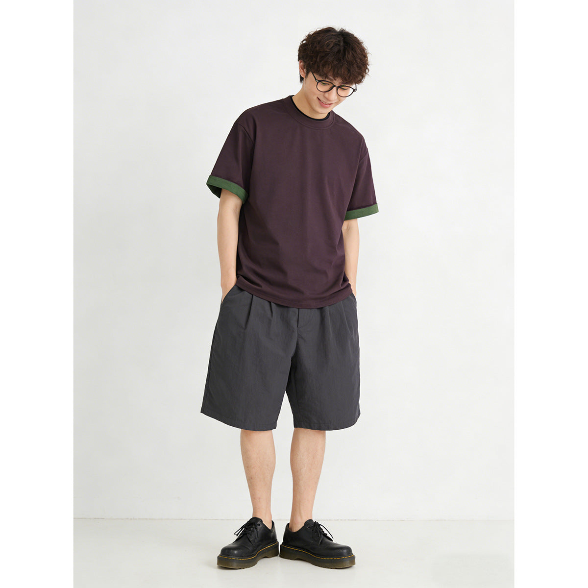 Model wearing a dark plum short-sleeve crew-neck T-shirt with green sleeve-cuff trim.