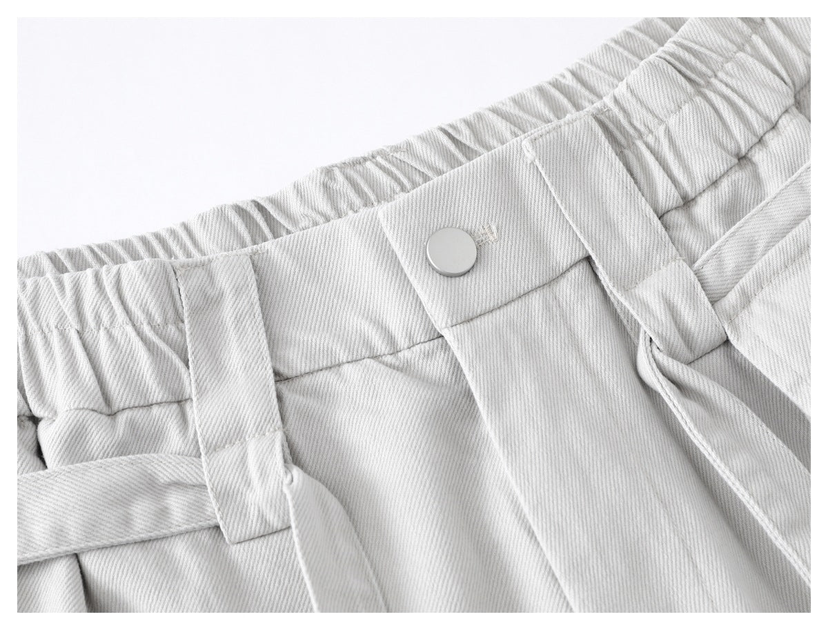 Close-up of light gray trousers showing the elastic waistband, silver button and belt loops.