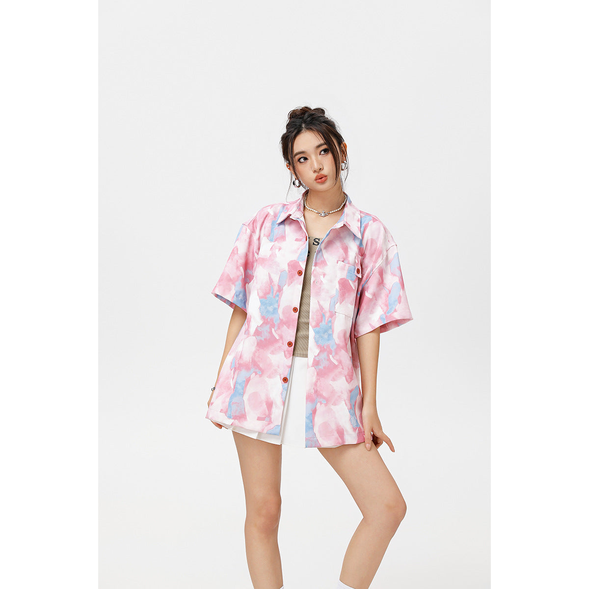 Model wearing an oversized pink and blue abstract-print short-sleeve button-up shirt over a white skirt.