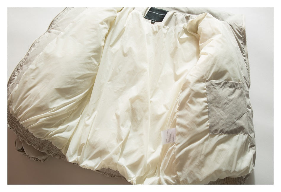 Inside view of a cream jacket laid flat, showing its lining, pocket, label, and elastic hem.