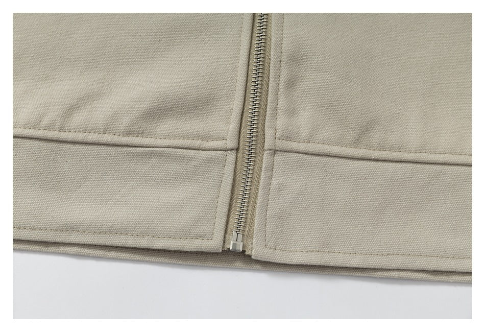 Close-up of the beige garment's lower hem, horizontal seams and centered metal zipper.