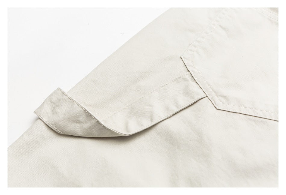 Close-up of a light ivory garment showing a stitched flap pocket and seam details.