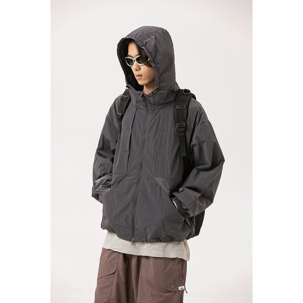 Model wearing a charcoal hooded zip jacket with angled front pockets and elastic cuffs.